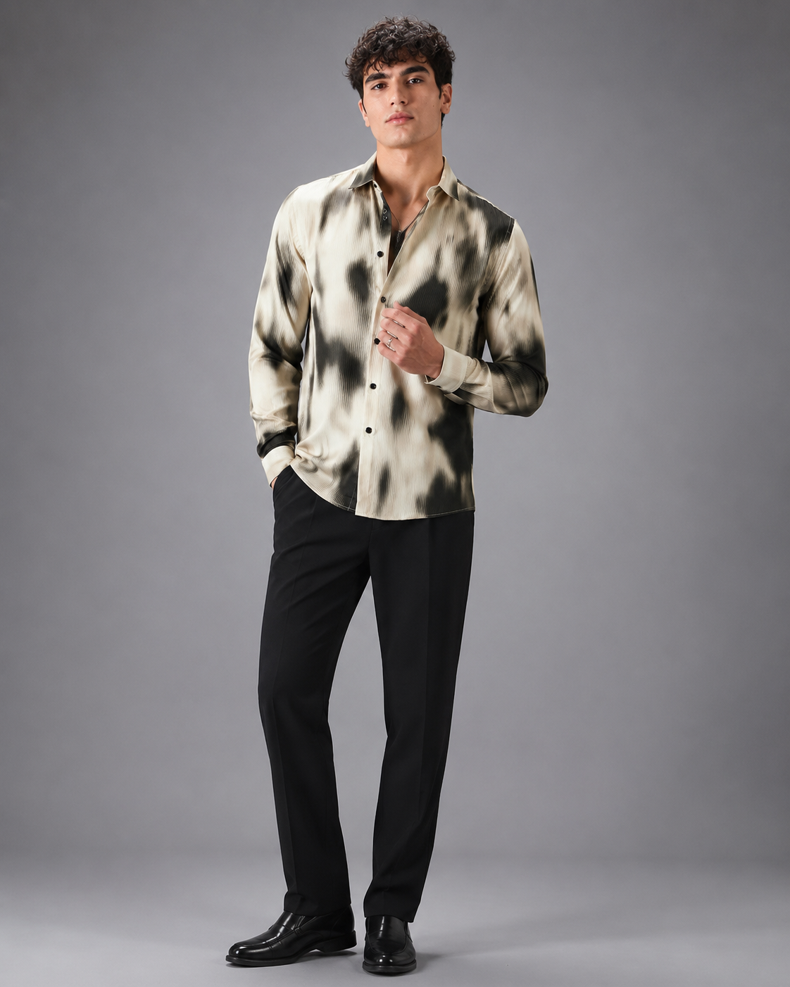 Man wearing a patterned shirt and black pants on a gray background